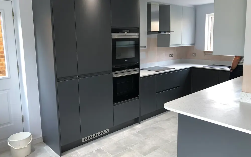 Fitted kitchen with dark grey handleless units, built-in ovens and a white worktop